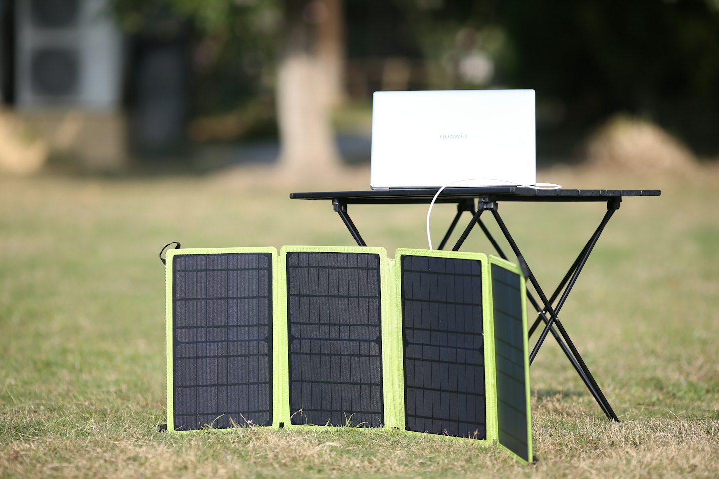 A laptop connects to portable solar panels on dry grass.